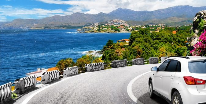 Ein weißes Auto fährt eine scharfe Kurve am Meer entlang