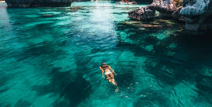 Frau schwimmt im Meer umgeben von Felsen