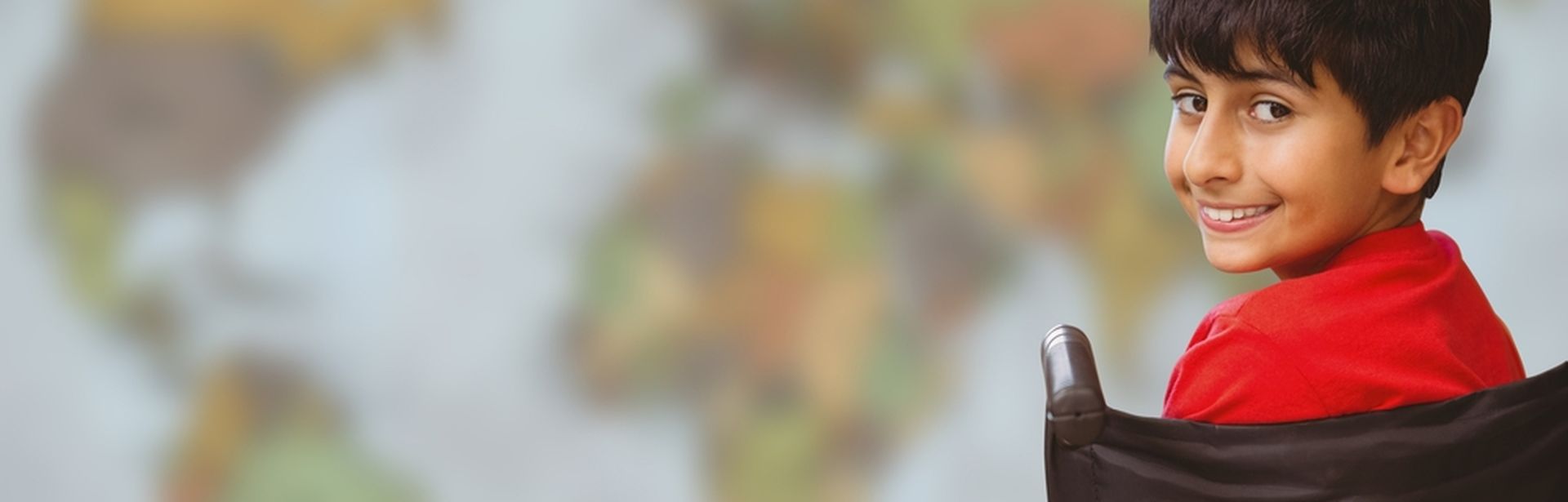 Ein Kind im Rollstuhl lächelt in die Kamera, im Hintergrund eine Weltkarte