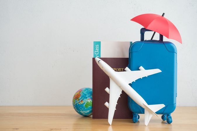 Auf einem Tisch steht ein Miniaturkoffer, Flugzeug und eine kleine Weltkugel mit einem Reisepass und einem Flugticket