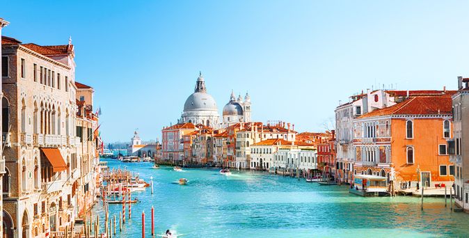 Blick auf den Canal Grande in Venedig, Italien. Links und rechts stehen historische Gebäude. Auf dem türkisblauen Wasser fahren kleine Boote.