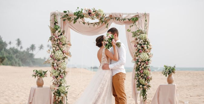 Ein Hochzeitspaar küsst sich unter einem Traubogen am Strand