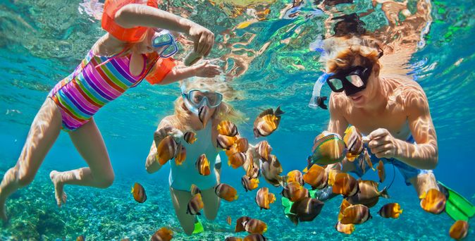 Drei Kinder schauen sich mit Taucherbrillen bunte Fische unter Wasser an
