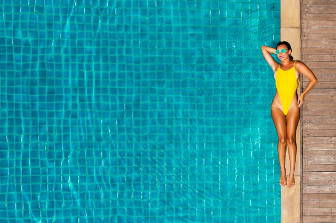 Ein großer Pool, am Rand liegt eine Frau im gelben Badeanzug und einer Sonnenbrille