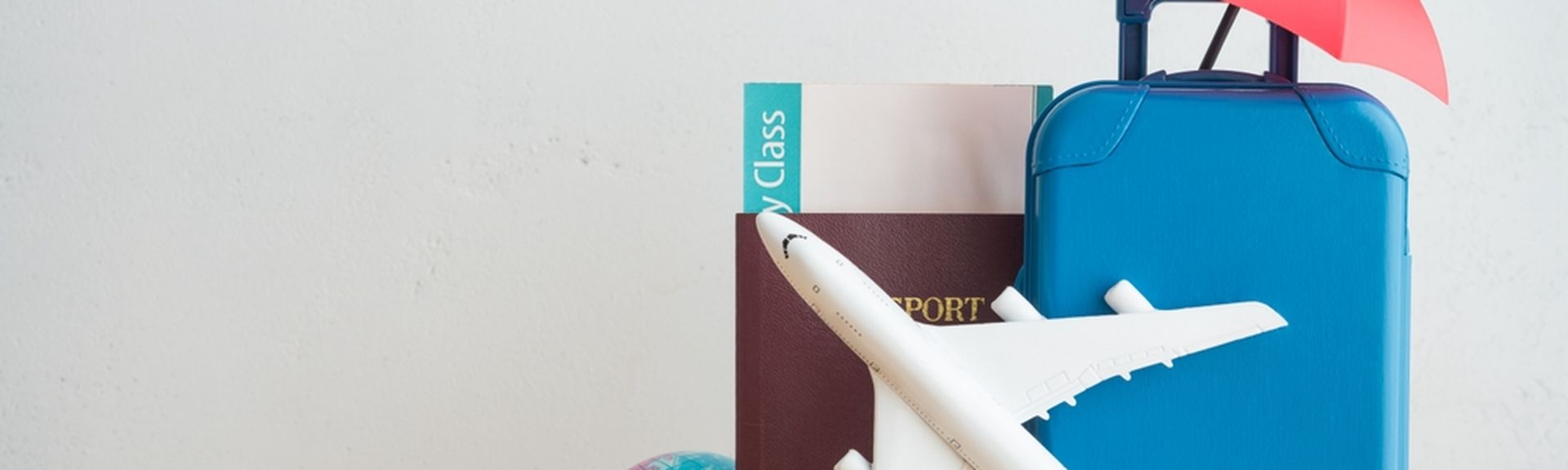 Auf einem Tisch steht ein Miniaturkoffer, Flugzeug und eine kleine Weltkugel mit einem Reisepass und einem Flugticket