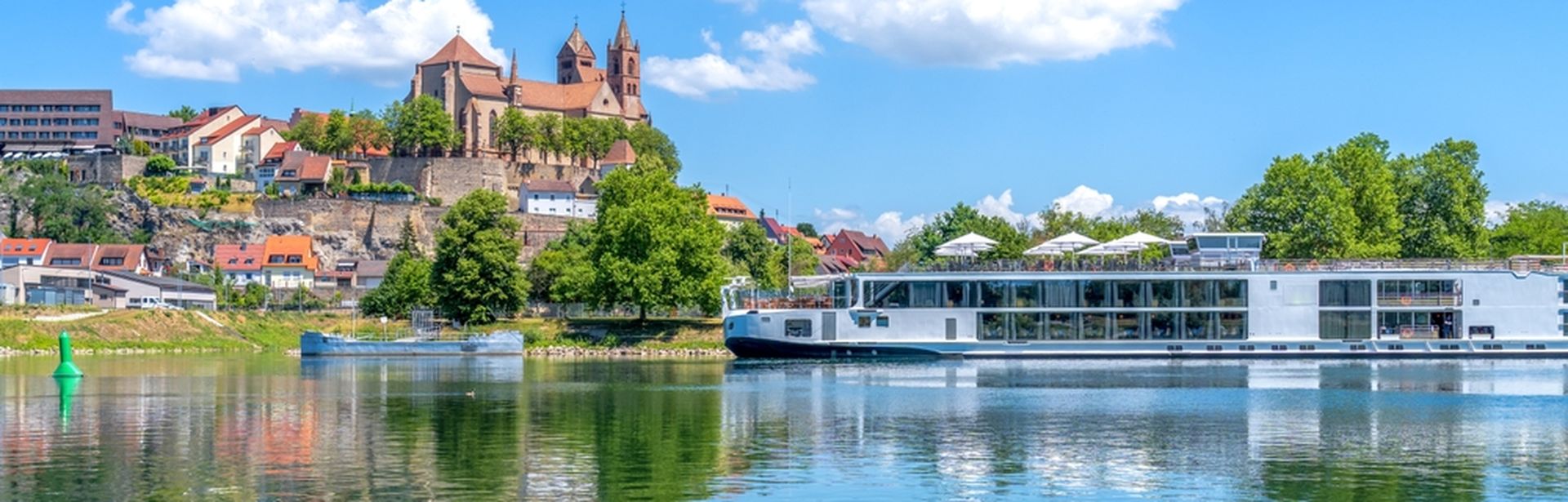 Flusskreuzfahrtschiff fährt entlang einiger Gebäude am Ufer bei Sonnenschein