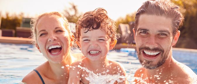 Eltern mit einem Kind spielen im Pool und lachen in die Kamera