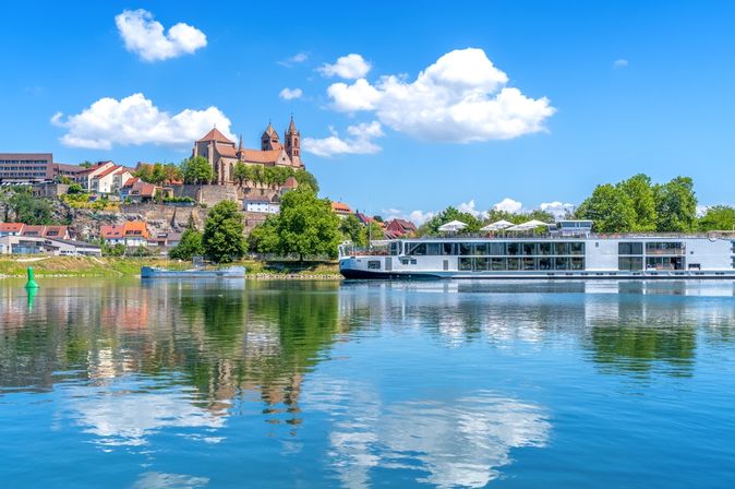 Flusskreuzfahrtschiff fährt entlang einiger Gebäude am Ufer bei Sonnenschein