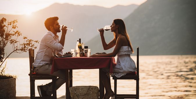 Eine Frau und ein Mann sitzen an einem Tisch am Wasser und trinken Wein