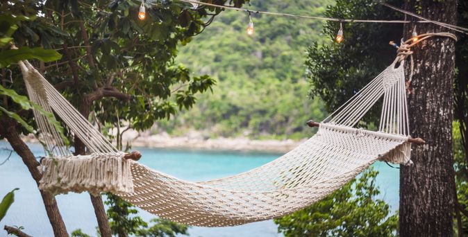 Hängematte zwischen zwei Bäumen, im Hintergund sieht man das Meer