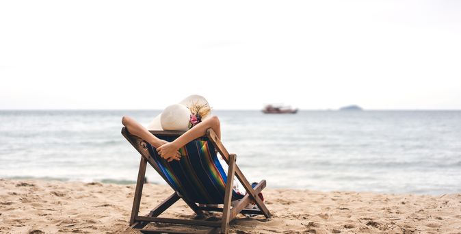 Person am Strand auf einer Liege schaut auf das Meer