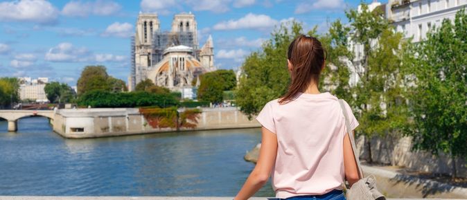 Eine Frau steht an einer Brücke und schaut auf das Wasser, im Hintergrund Bauwerke