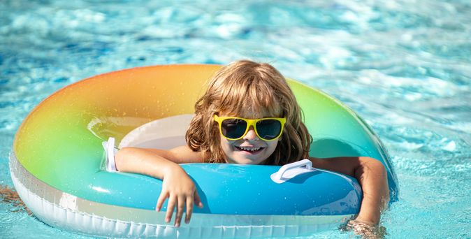 Ein Kind mit einer Sonnenbrille in einem bunten Poolring