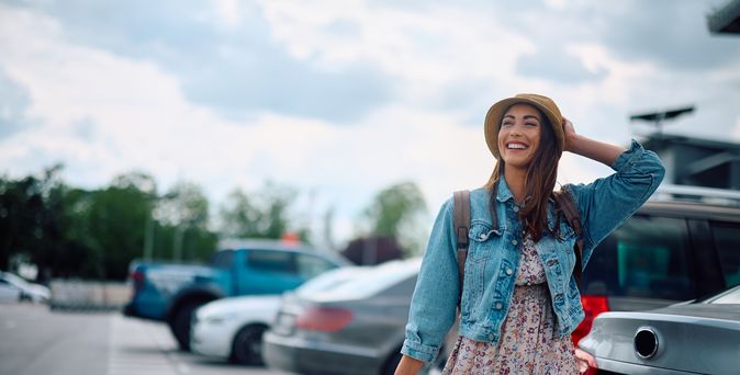Eine lachende Frau zieht ihren Koffer über einen Parkplatz