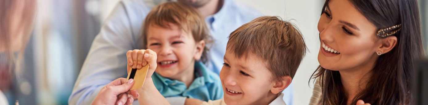 Eine Familie mit zwei Kindern beim Check-In in, Die Rezeptionistin reicht dem kleinen Kind die Zimmerkarte