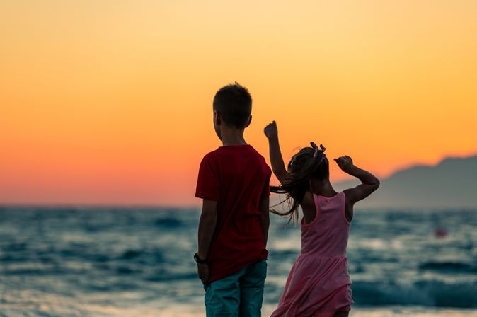 Zwei Kinder schauen bei Sonnenuntergang aufs Meer