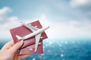 Eine Hand hält vor einem blauen Hintergrund zwei Reisepässe und ein Miniaturflugzeug hoch