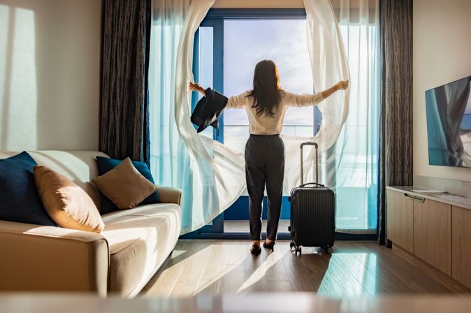 Eine Frau öffnet die Vorhänge ihres modernen Hotelzimmers