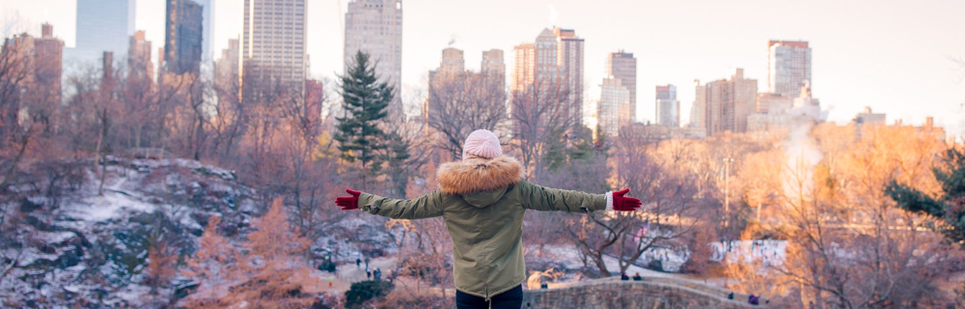 Eine Frau steht mit ausgebreiteten Armen auf einem Vorsprung vor einem schneebedeckten Park