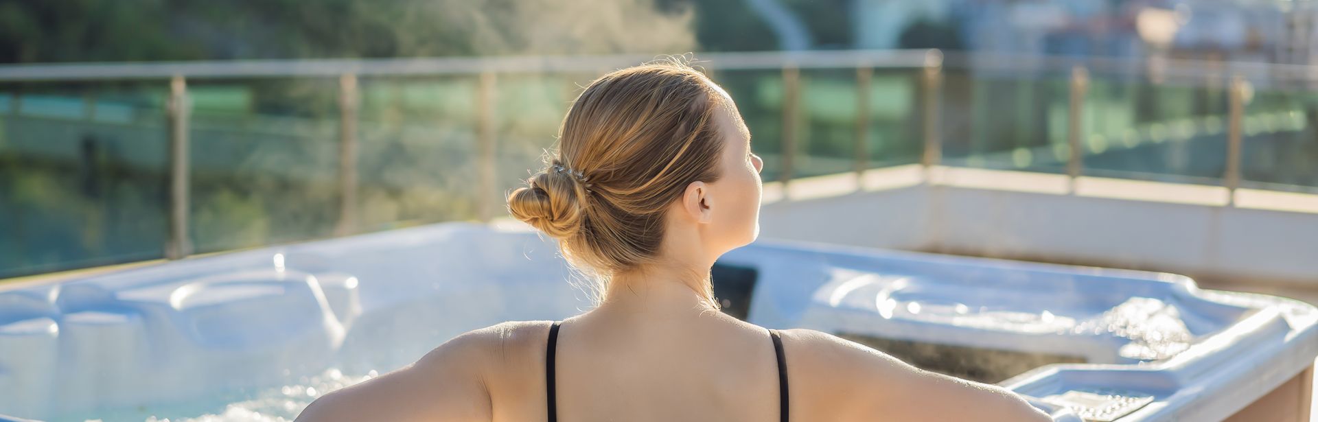 Eine Frau sitzt entspannt in einem Whirlpool, Die Sonne scheint und sie ist umgeben von Natur