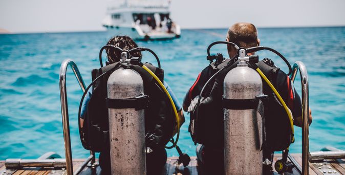 Taucher sitzen mit Tauchausrüstung am Wasser