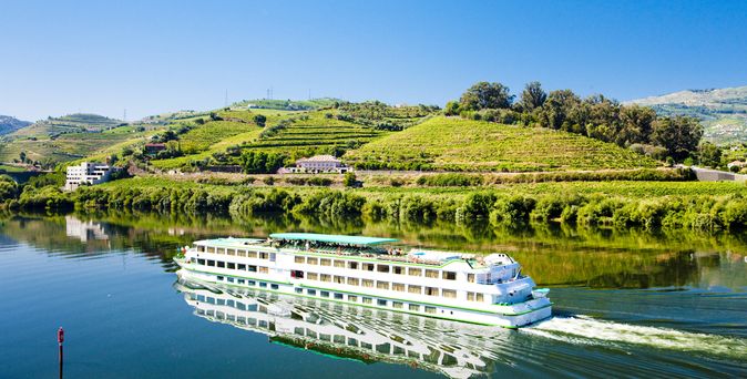 Flusskreuzfahrtschiff, dass durch eine hüglige, grüne Landschaft fährt