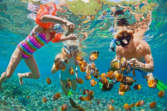 Drei Kinder schauen sich mit Taucherbrillen bunte Fische unter Wasser an