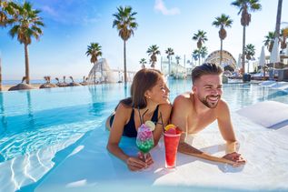 Lachendes Paar trinkt Cocktails, während sie im Pool liegen