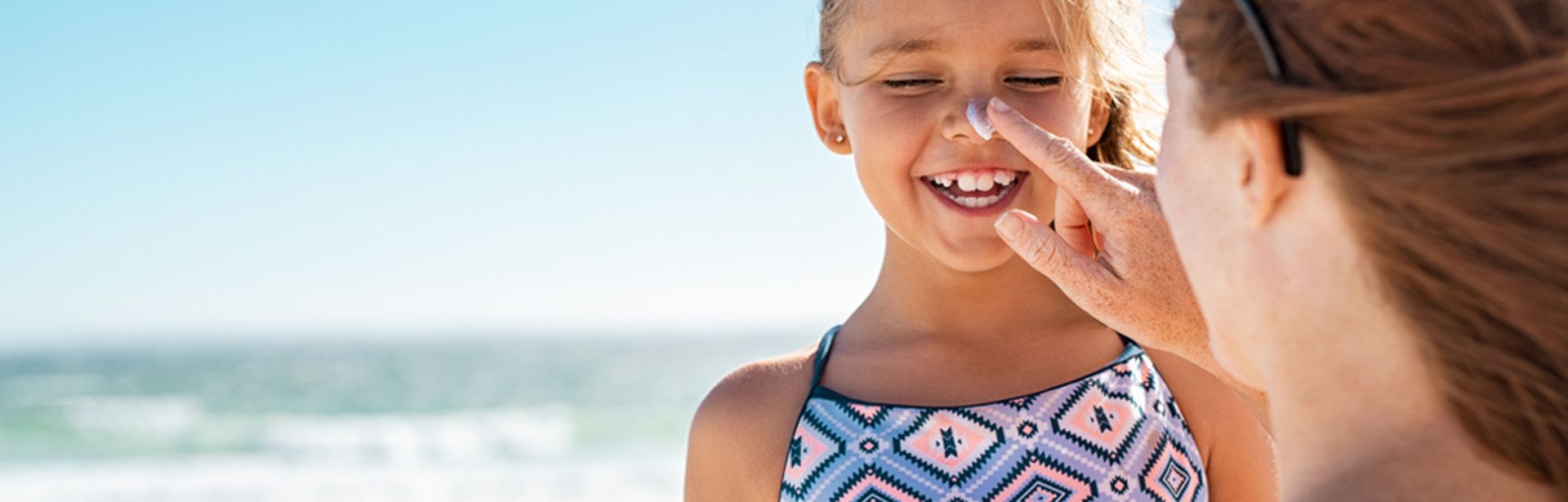 Mutter cremt ihre Tochter mit Sonnencreme im Gesicht ein