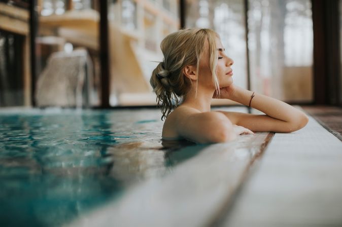 Frau lehnt am Rand eines indoor Pools und hat die Augen geschlossen