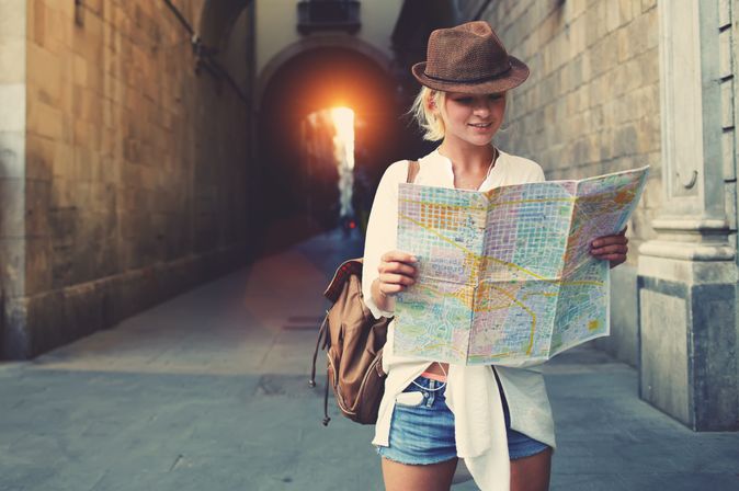 Eine Frau mit einer braunen Mütze und einem Rucksack schaut interessiert auf eine Stadtkarte.