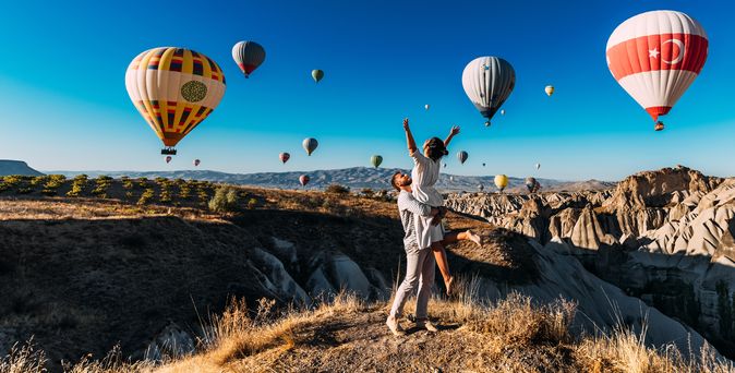 Ein Mann trägt eine Frau im Arm, um Sie herum schweben Heißluftballons durch die Luft