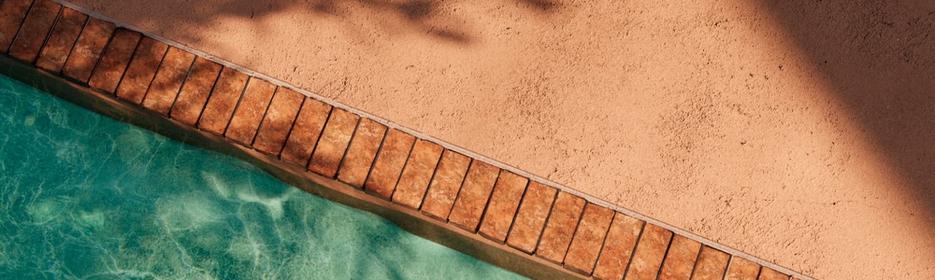 Aus der Vogelperspektive fotografierter Poolausschnitt: Der Rand eines Pools ist links im Bild sichtbar, daneben ein heller Steinboden.