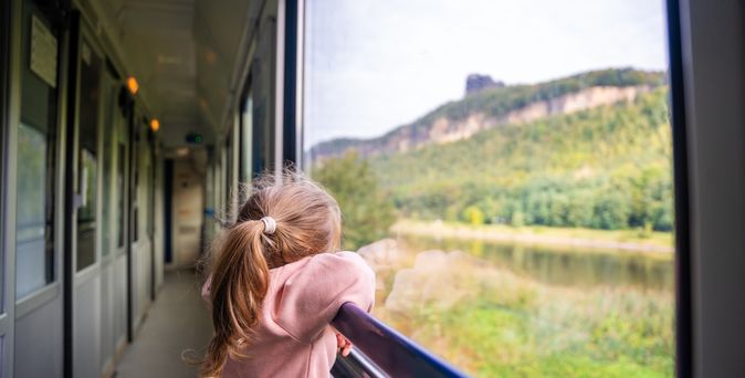 Ein Kind steht am Fenster in einem Zug und schaut auf die grüne Landschaft