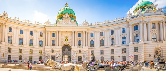 Pferdekutsche vor der Hofburg in Wien, Österreich, an einem sonnigen Tag. Im Hintergrund laufen viele Touristen über den Platz.