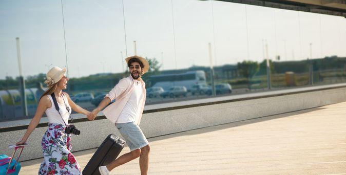 Ein Paar läuft mit Koffern aufgeregt einen Weg entlang