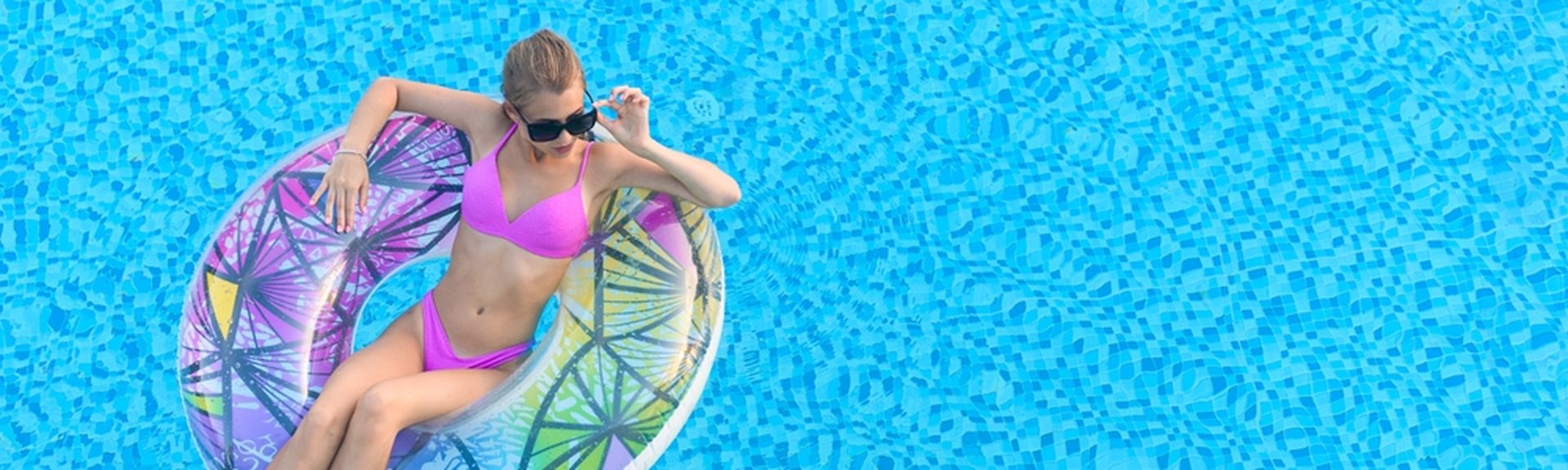 Eine Frau in einem pinken Bikini sitzt in einem Pool in einem bunten Poolfloatie