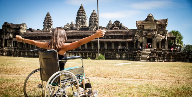 Frau im Rollstuhl vor einem Tempel und hebt die Arme