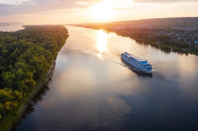 Flusskreuzfahrtschiff, dass bei Sonnenuntergang auf einem Fluss fährt