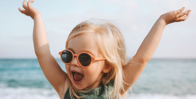 Mädchen mit Sonnenbrille streckt die Arme in die Luft und lächelt