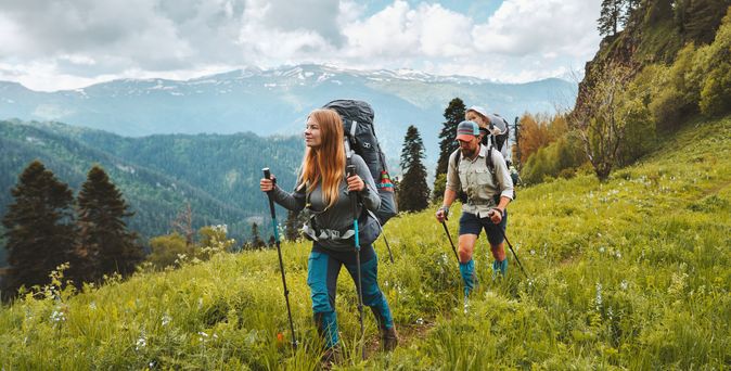 Zwei Personen wandern mit Nordic Walking Stöckern durch eine Wiese