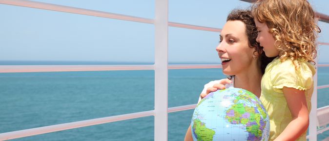 Mutter und Kind schauen über das Geländer eines Kreuzfahrtschiffes und halten einen Globus