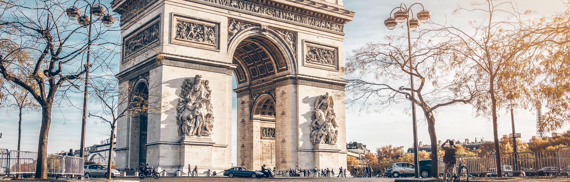 Der Arc de Triomphe im Herbst. im Vordergrund liegen braune Blätter auf dem Boden.