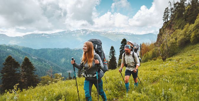Zwei Personen wandern mit Nordic Walking Stöckern durch eine Wiese