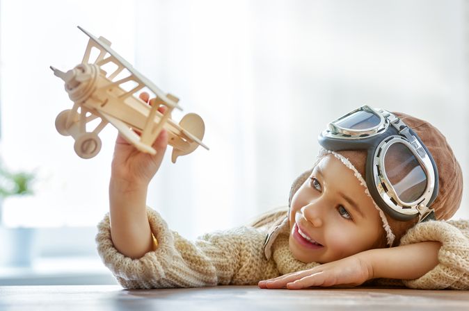 Junge trägt einen Fliegerhelm und spielt mit einem Modellflugzeug