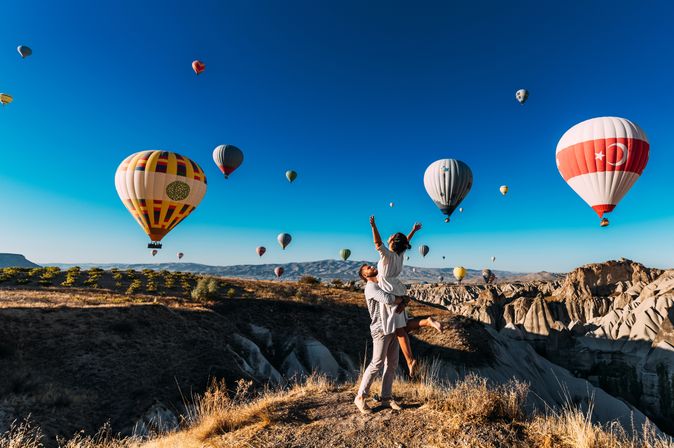 Ein Mann trägt eine Frau im Arm, um Sie herum schweben Heißluftballons durch die Luft