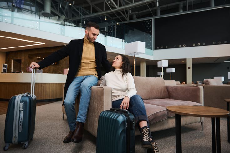 Eine Frau und ein Mann sitzen mit Koffern in einer Lobby und schauen sich an