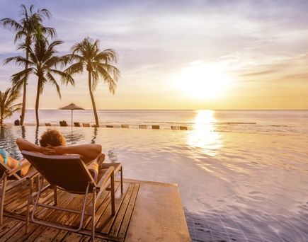 Zwei Personen liegen auf Liegen am Pool und schauen sich den Sonnenuntergang an