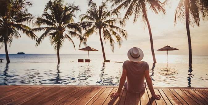 Mann sitzt auf einem Steg am Wasser und schaut in die Sonne