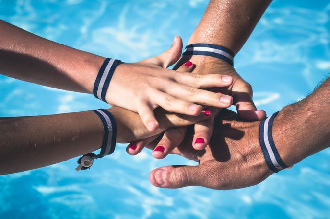 Vier Hände mit Armbändern aufeinander über einem Pool